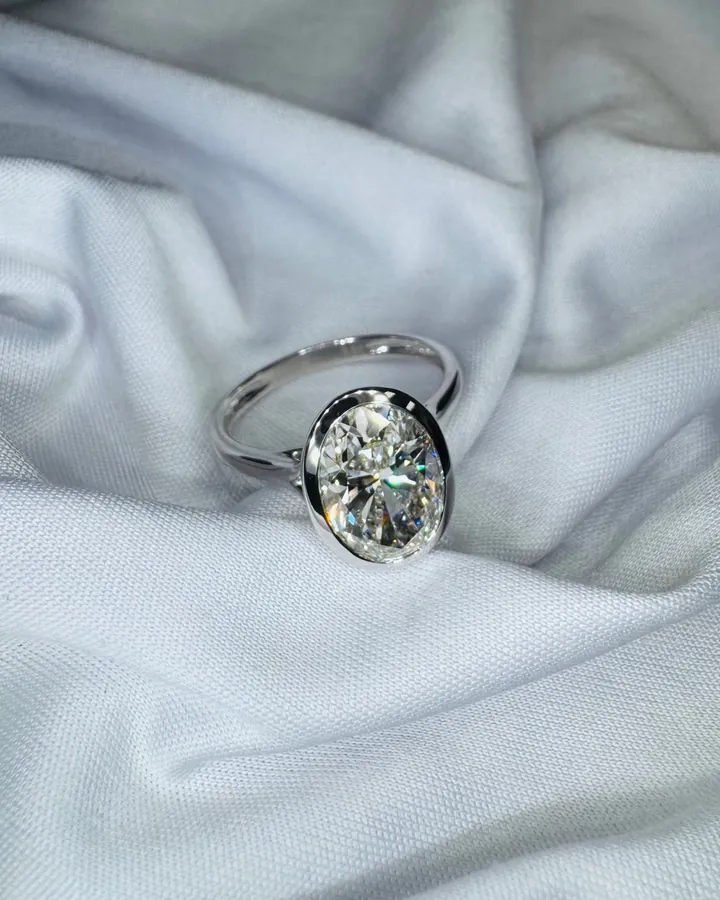 Bezel-set oval diamond solitaire in polished white metal