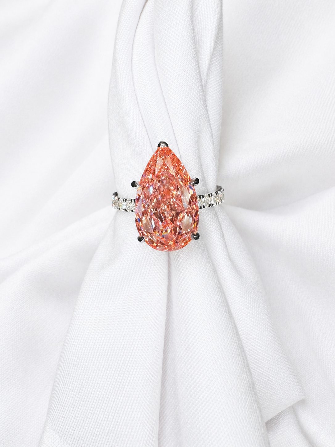 Pear-shaped pink-orange colored diamond solitaire with a pavé band