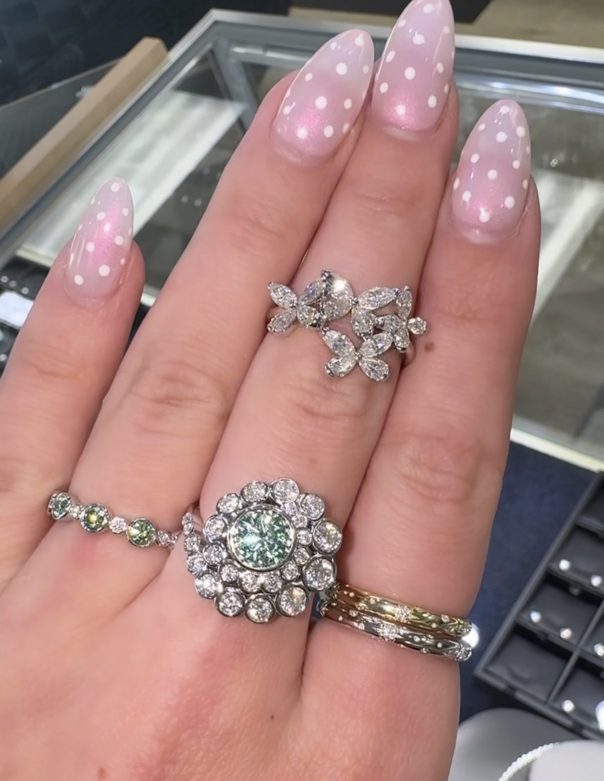 Hand wearing floral cluster and green-stone diamond rings