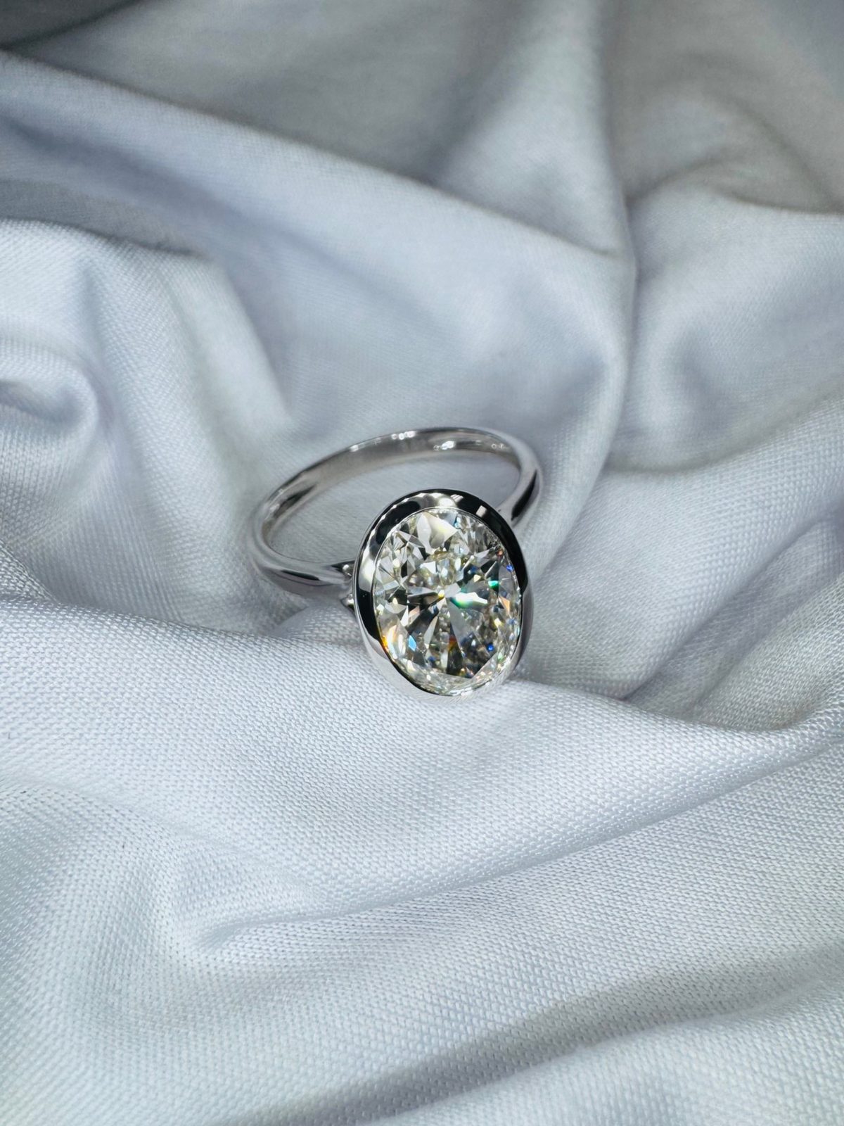 Bezel-set oval diamond solitaire in white gold on soft fabric