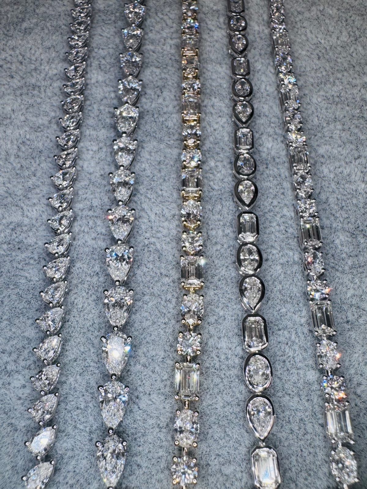 Several diamond tennis bracelets in mixed cuts laid on gray velvet